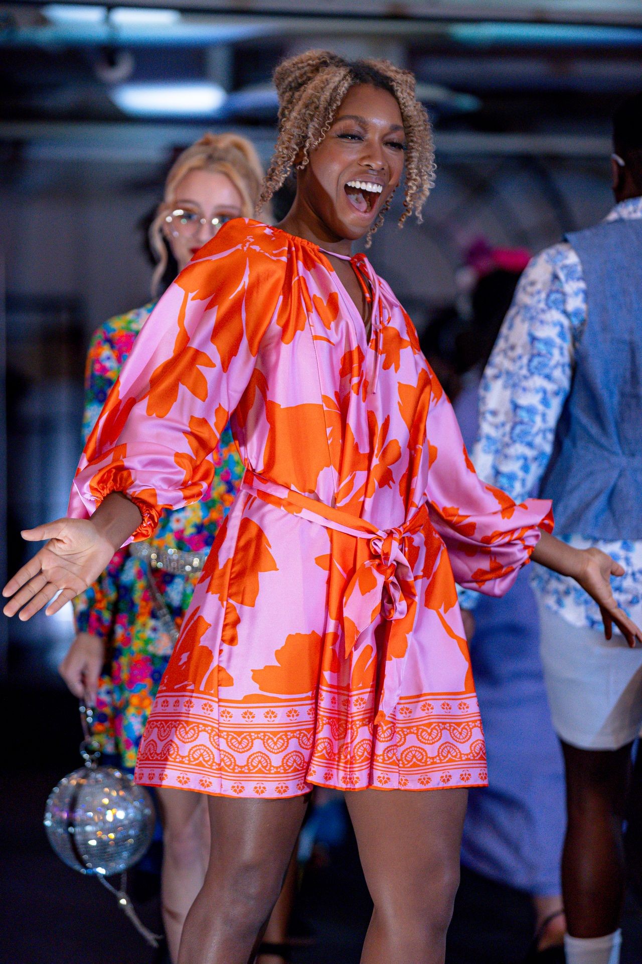 Person in a vibrant orange and pink floral dress on a lively runway.